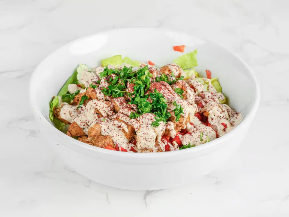 Chicken Shawarma - Tender marinated chicken topped with creamy tahini sauce, sumac, and fresh herbs over a bed of crisp greens.